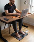 Man working at a laptop with bare feet on the EMS foot massager mat underneath