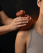 Therapist pressing a warm herbal massage ball onto a woman's shoulder