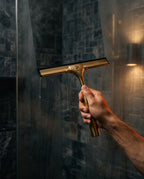 Hand using the brass squeegee to wipe water off a wet shower glass door