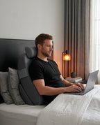Man using laptop in bed leaning on gray ergonomic bed backrest