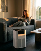 Air purifier on a living room floor as a woman reads on the couch