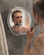 Man shaving his face in the fog-free shower mirror amid steam in a tiled shower