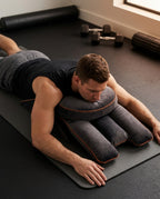 Man lying face-down on the grey support pillow on a gym recovery mat