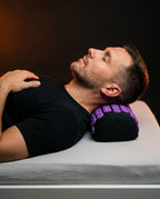 Man resting his neck on the purple acupressure pillow on a bed