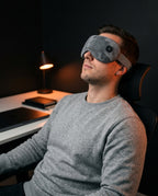 Man reclining in an office chair wearing the grey heated eye massager on a break