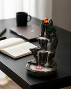 Incense holder releasing waterfall smoke on a desk with laptop and book