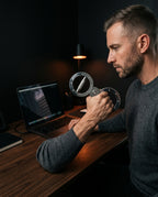 Man training his grip with the steel trainer at an office desk by a laptop
