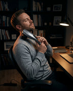 Man relaxing at a desk using the handheld massager on his neck and shoulder