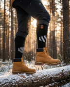 Heated socks worn with hiking boots on a snowy log outdoors