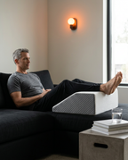 Man on a sofa with feet raised on the leg elevation wedge for recovery