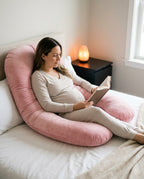 Pregnant woman reading supported by a pink U-shaped pregnancy pillow