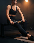 Woman rolling the massage stick across her thigh on a dim gym bench