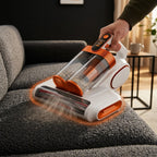 Person vacuuming a grey upholstered sofa with the handheld fabric cleaner
