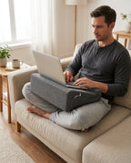 Man using a laptop balanced on the grey lap cushion on a sofa