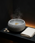 Steaming stone aroma bowl with oil drops on a dark spa bathroom shelf
