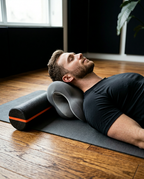 Man lying on a yoga mat with the neck cushion under his neck and a foam roller