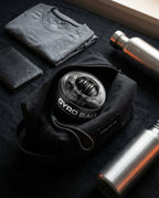 Gyro ball trainer in a travel pouch beside a t-shirt and water bottles, flat lay