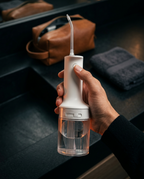 Hand holding the portable water flosser beside a leather travel bag