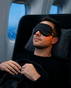 Man resting on an airplane wearing the black silk eye mask by the window