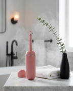 Pink personal hygiene bottle and cap on a marble bathroom counter with eucalyptus