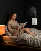 Woman reading in bed near the wall-mounted diffuser releasing fragrance mist