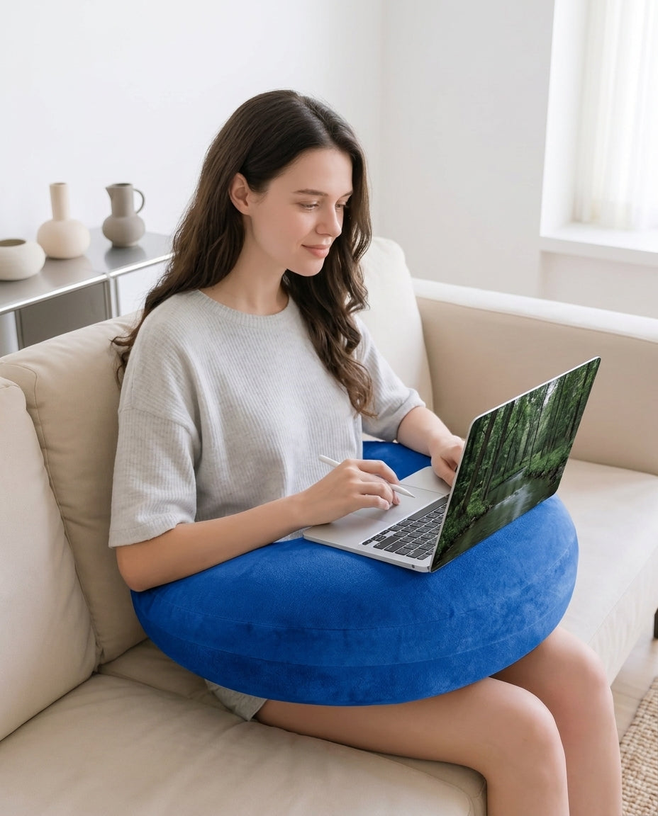 Woman using a laptop balanced on the blue lap pillow on a couch