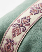 Macro of embroidered ikat trim in purple and rose on sage green linen pillow border