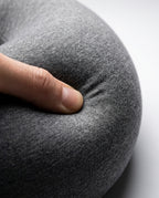 Thumb pressing into the grey travel neck pillow, showing memory foam softness