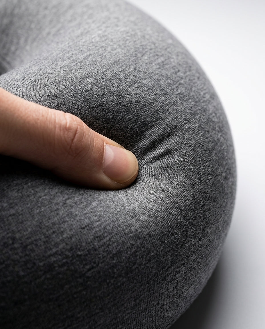 Thumb pressing into the grey travel neck pillow, showing memory foam softness