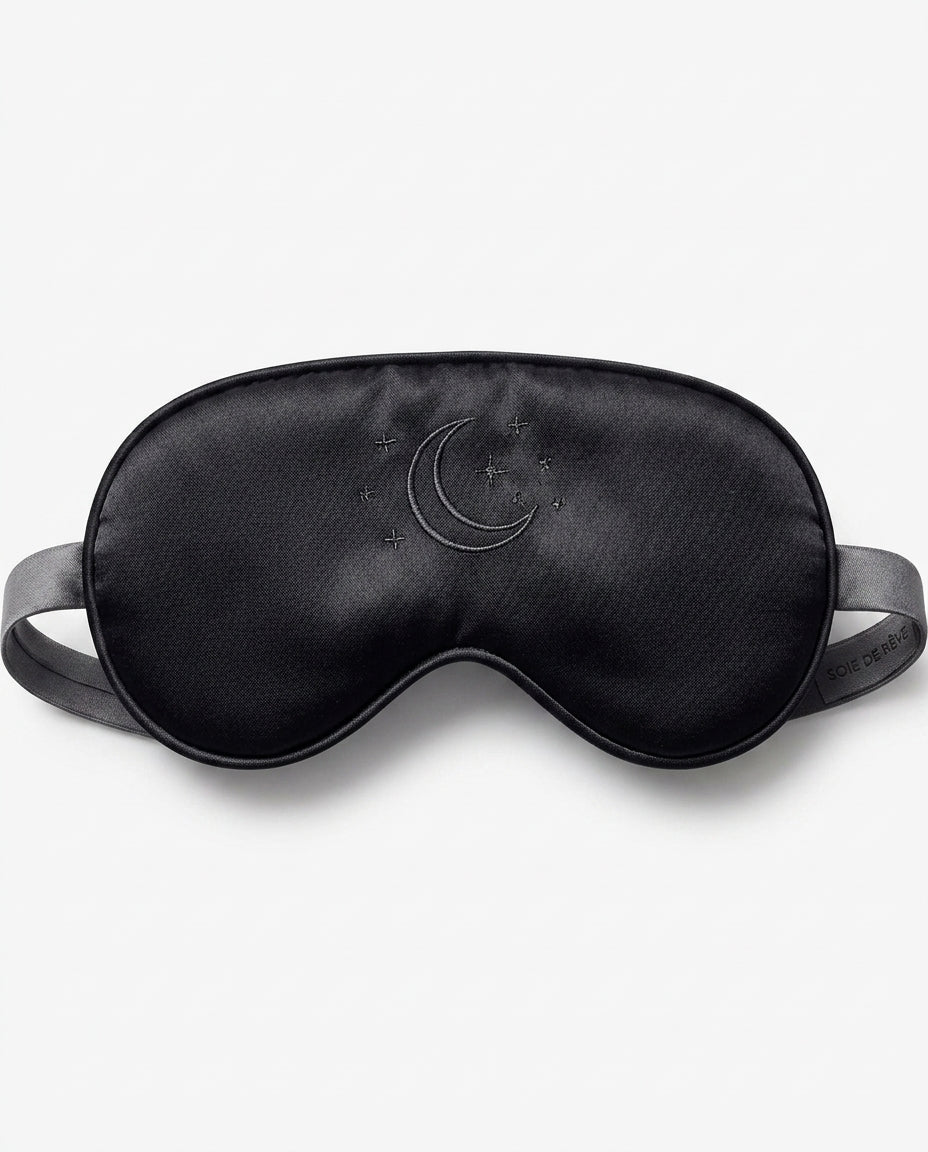 Black silk eye mask with embroidered crescent moon, showing smooth weave
