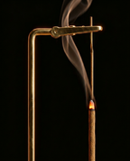 Macro of the brass suspended arm gripping a lit incense stick with rising smoke