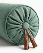 Close-up of the gathered bolster end with covered button and two leather tassels on green linen