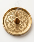 Lotus-engraved brass incense tray holding a burning cone, top view