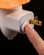 Finger turning the rotary dimmer dial on the salt lamp's white plug base