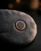 Close-up of the eye massager's round power button glowing orange