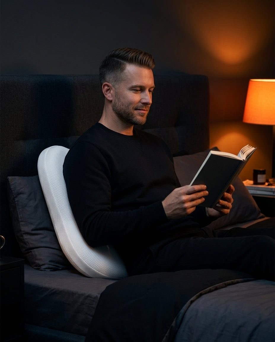 Man reading in bed with the V-shaped pillow supporting his back
