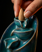 Hand placing a backflow incense cone on top of the waterfall burner