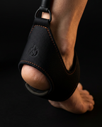 Padded neoprene foot strap with orange stitching worn on a bare foot