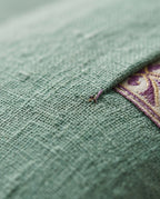 Macro detail of the breathable sage green linen weave beside the embroidered trim