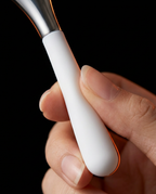 Hand gripping the matte white silicone handle of the steel eye massage tool