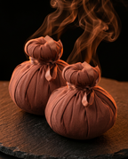 Pair of warm herbal massage balls with steam rising on dark slate