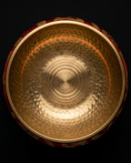Top-down view inside the hammered brass singing bowl on its red cushion