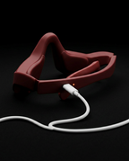 Burgundy eye massager with white USB charging cable plugged in