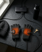 Heated gloves charging via USB-C beside a beanie, bottle and keys on slate