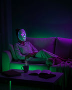 Person reclining on a couch wearing the LED mask in green and purple light