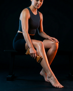 Seated woman rolling the wooden massage roller down her calf to release leg muscles