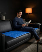Man reading on a black leather sofa while sitting on the blue cooling gel pad
