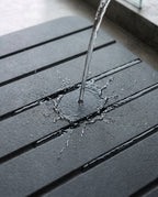 Water poured onto the dark bath mat showing the channel grooves draining