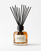Clear glass reed diffuser with amber oil and black reeds on white