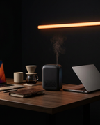 Black diffuser misting on a wood desk beside a laptop and coffee maker